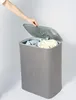 A hand is shown opening the lid of a grey laundry basket filled with clothes. Produktbild-Vorschau