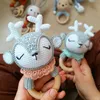 Two crocheted deer rattles are held by hands, with other baby toys in the background. Produktbild-Vorschau
