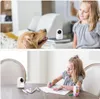 A collage of two images showing a Reolink E Series E321 indoor camera in use. The top image shows the camera next to a golden retriever and a young girl. The bottom image shows the camera on a table next to a young girl drawing. Náhled obrázku produktu