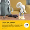 A Medela Harmony hand breast pump is shown on a wooden surface next to a bag, sunglasses, and keys, with a yellow couch in the background. Podgląd zdjęcia produktu