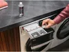 A person is adding liquid from a small cap into a washing machine detergent drawer. Produktbild-Vorschau