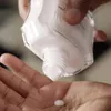 A hand is holding a bottle of lotion and dispensing it into the palm of the other hand. Produktbild-Vorschau