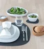 A table setting with a placemat, plates, cutlery, a glass of water, and a salad. Produktbild-Vorschau