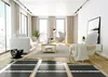 A modern living room with a sofa, armchair, coffee table, and large windows, featuring underfloor heating elements in the foreground. Produktbild-Vorschau