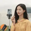 A woman is holding a selfie stick with a phone attached, outdoors. Voir les images du produit