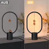 A split image showing a desk lamp in two states: off and on. The lamp has a black base and an oval frame with two copper spheres that levitate and connect via magnetic force when the lamp is on. Produktbild-Vorschau