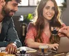 Two people are sitting at a table, one is working on a laptop and the other is looking at them and smiling. There are coffee cups on the table. Podgląd zdjęcia produktu