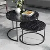 A set of two round nesting coffee tables with a black marble-like top and black metal legs, placed on a light gray floor. A white vase with white flowers and a book are on the larger table. Voir les images du produit