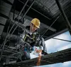 A construction worker is using an angle grinder on a metal beam at a height. Produktbild-Vorschau