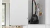 A black Bosch vacuum cleaner is stored in a white cabinet along with an umbrella and a dustpan and brush. Produktbild-Vorschau