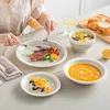 A person is eating a meal with a steak, vegetables, soup, salad, and dessert, served on a set of ceramic dishes. Produktbild-Vorschau