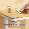 A hand wiping a spill from a wooden desk surface next to a coffee cup. Produktbild-Vorschau
