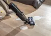 A person is using a wet dry vacuum cleaner to clean up a spill on a wooden floor next to a bed. Voir les images du produit