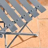 Close-up of a gray metal folding bistro table and chairs set on a brick patio. Produktbild-Vorschau