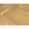 A roll of wood-grain patterned contact paper is shown unrolling onto a surface of the same pattern. Produktbild-Vorschau