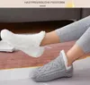 Person, die graue gestrickte Hausschuh-Socken mit weißem Fleece-Innenfutter trägt, ein Fuß ruht auf dem anderen auf einem Teppich Náhľad obrázku produktu