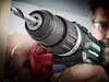 A close-up shot of a person using a cordless drill to drill into a piece of wood. Sawdust is flying. Produktbild-Vorschau