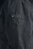 A close-up view of a dark-colored jacket with a small pocket detail. Produktbild-Vorschau