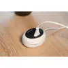 A white power strip with two USB ports is plugged into a wall socket on a wooden surface. Produktbild-Vorschau