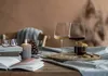 A cozy scene with two wine glasses, a lit candle, books, and cookies on a table. Náhled obrázku produktu