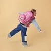 A young girl wearing a backpack is balancing on one leg against a plain background. Náhled obrázku produktu