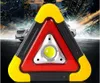 A warning triangle with an LED light in the center, set against a blurred background of city lights and cars. Náhled obrázku produktu