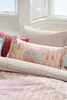 A close-up view of a bed with several pillows and bedding. Produktbild-Vorschau
