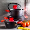 A set of black pots with red handles and lids, arranged in a stack, with tomatoes and spaghetti in the foreground. Náhled obrázku produktu