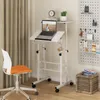 A white adjustable standing desk with a laptop on it, next to an orange and white office chair. A pegboard with various items is on the right wall. Podgląd zdjęcia produktu