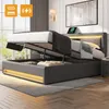 A modern bedroom with a grey upholstered bed frame, partially open to reveal storage space. The bed has LED lighting along the base and headboard. A tablet is placed on the headboard. Náhled obrázku produktu