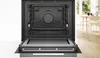 An open Bosch oven with its interior visible, set against a white background with a blurred kitchen scene in the background. Produktbild-Vorschau