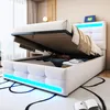 A white upholstered bed with storage is shown with the mattress lifted, revealing stored items. Blue LED lights illuminate the base of the bed. Náhľad obrázku produktu