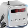 A white and silver mini speaker with a digital display and buttons, shown with attached cables. Produktbild-Vorschau