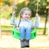 A young girl is happily swinging on a green swing in an outdoor setting with trees and foliage in the background. Náhľad obrázku produktu