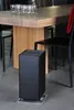 A black air purifier sits on a gray floor in front of a wooden dining table. Podgląd zdjęcia produktu