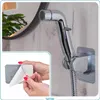 A hand is shown peeling the backing off of a self-adhesive holder for a bidet spray head, which is mounted on a wall. Anteprima dell’immagine prodotto
