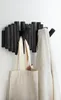A black coat rack with multiple pegs is mounted on a white wall. A beige tote bag hangs from one peg, and a textured cream-colored blanket is draped over another. Anteprima dell’immagine prodotto
