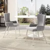 Two gray velvet dining chairs with silver metal legs are placed around a white round dining table in a well-lit room with a large window overlooking a garden. Podgląd zdjęcia produktu