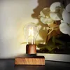 A levitating light bulb with a wooden base, placed on a dark surface with a blurred background of white orchids. Produktbild-Vorschau