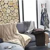A cozy living room scene with blankets draped over a sofa, a wood-paneled wall, and a clothing rack in the background. Produktbild-Vorschau