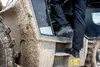 A person is stepping into a muddy construction vehicle, wearing black safety boots. Produktbild-Vorschau