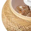A close-up view of a woven bamboo lampshade with a light bulb inside. Produktbild-Vorschau