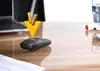 A black presentation clicker and two AA batteries are shown on a wooden desk, with a laptop in the background. A yellow arrow graphic points from the batteries to the clicker. Podgląd zdjęcia produktu