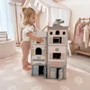 A young child plays with a wooden toy police and fire station set in a brightly lit room with a canopy and clothing rack in the background. Anteprima dell’immagine prodotto