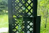 A close-up view of a black lattice trellis with a vine growing on it, set against a blurred background of greenery and trees. Produktbild-Vorschau