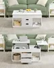 A white lift-top coffee table with storage, shown both closed and open, in a living room setting with a green sofa. Náhled obrázku produktu
