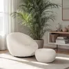 A modern living room setting with a white bouclé armchair and matching ottoman. Produktbild-Vorschau