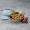 A stainless steel serving pan filled with ratatouille, with a glass lid and a red pepper and herbs nearby, set on a textured gray surface. Podgląd zdjęcia produktu