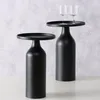 Two black side tables with wine glasses on one of them, against a textured gray and white background. Produktbild-Vorschau