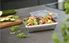 A stainless steel food container filled with skewers of vegetables and tofu sits on a kitchen counter, with sliced zucchini and basil leaves nearby. Produktbild-Vorschau